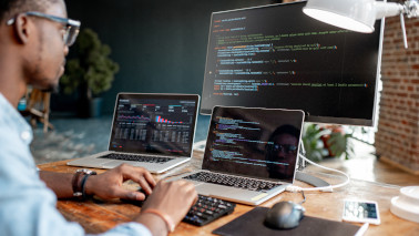 Programmierer sitzt an seinem Arbeitsplatz mit 3 Monitoren und schreibt an einem Programmcode. Der Fokus liegt auf den Monitoren. Programmierer sitzt an seinem Arbeitsplatz mit 3 Monitoren und schreibt an einem Programmcode. Der Fokus liegt auf den Monitoren.